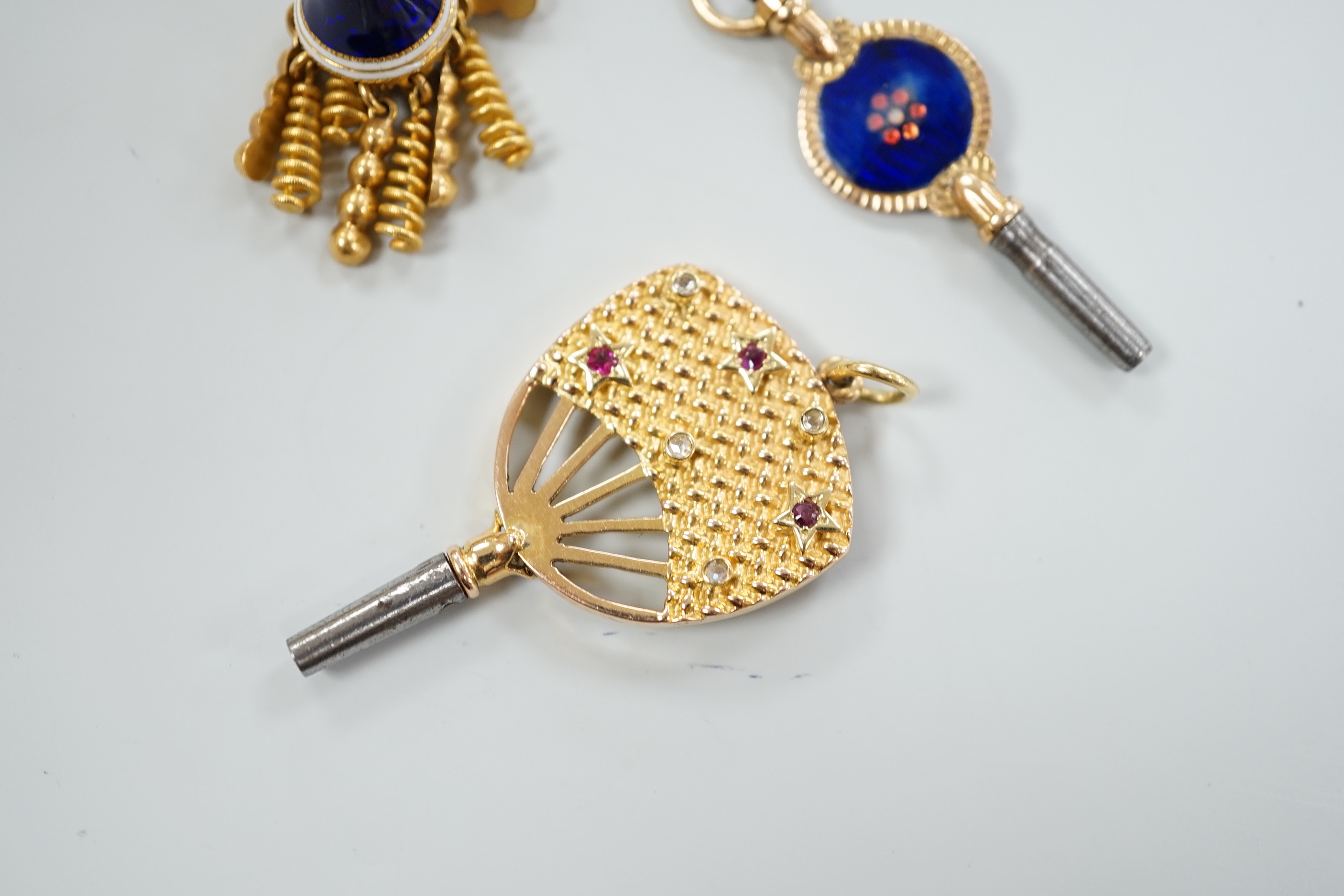 An early 20th century yellow metal (stamped 15), ruby and diamond set watch key, 39mm, together with a three colour enamelled watch key and an enamelled tassel charm.